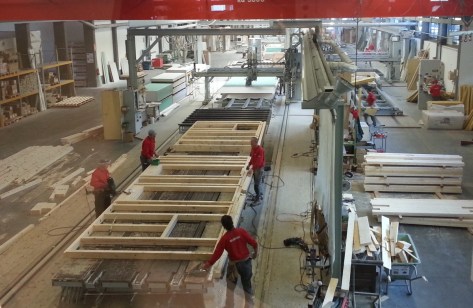 foto 1 Una volta eseguita la progettazione esecutiva dell’edificio da realizzare, tutte le parti in legno (travi, montanti, tavolati, ecc.) vengono realizzate con macchine a controllo numerico che tagliano, forano, fresano, predispongono gli incastri, il tutto è realizzato in modo perfetto e computerizzato. A questo punto tutti i pezzi sono stati numerati e sono pronti per il montaggio che avviene effettuato secondo il progetto e senza alcuna possibilità di errore da manodopera specializzata sui dei grandi banchi automatizzati che consentiranno di movimentare le pareti per le successive fasi di lavorazione.